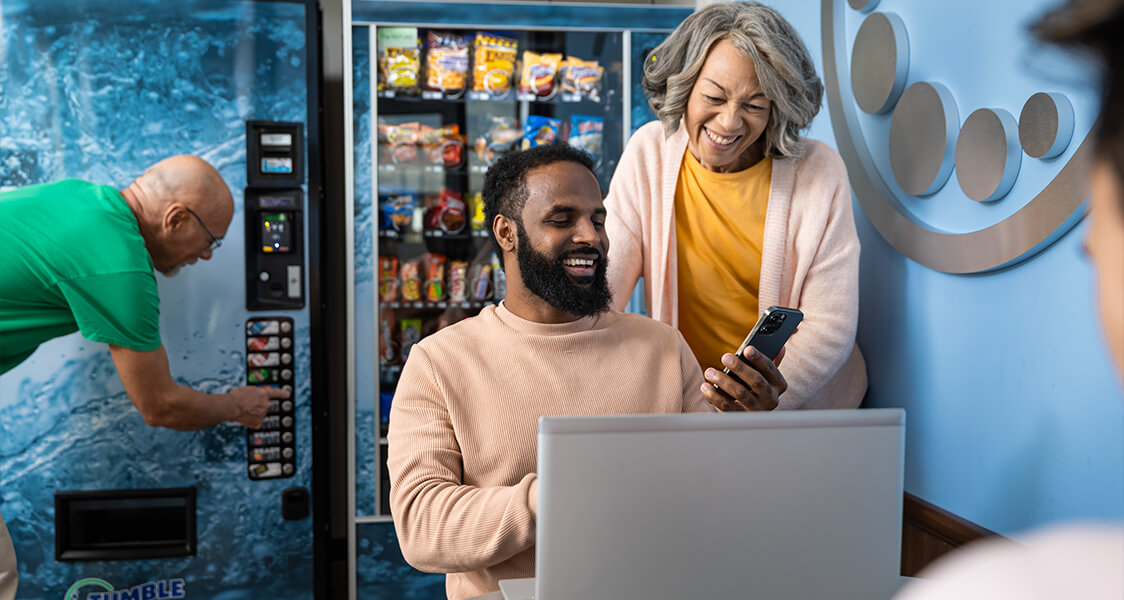 a man on his laptop smiling as an older woman chats with him